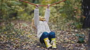 穿黄色靴子的小女孩在秋天公园的操场上玩绳子